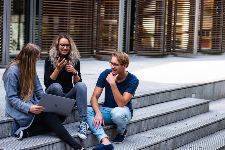 Three young professionals having a chat about changes to HECS home loan rules while sitting on outdoor steps.