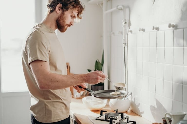 Man making pancakes in a sunlit kitchen, capturing the casual morning routine as he reflects on the RBA rate decision and his home loan