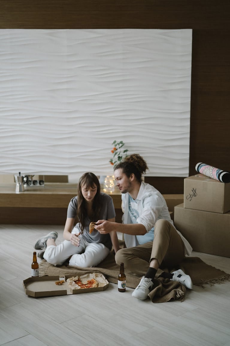 A happy couple enjoys pizza in their newly bought apartment with moving boxes around after figuring out how much deposit they would need in Perth