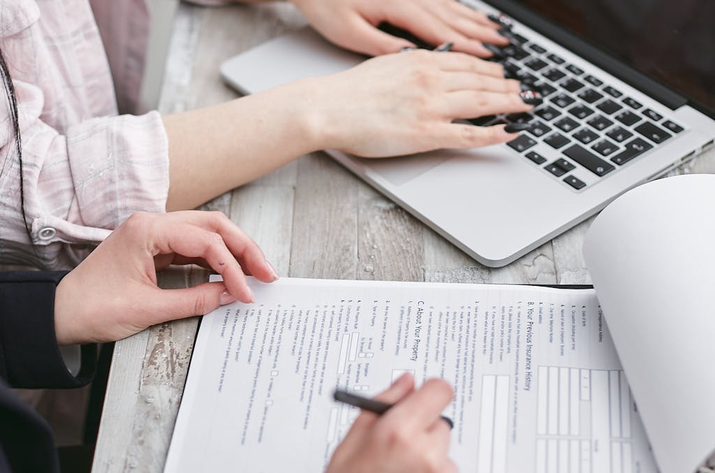 Close-up of hands typing on a laptop and reviewing home loan documents, focused on finance and legal tasks.