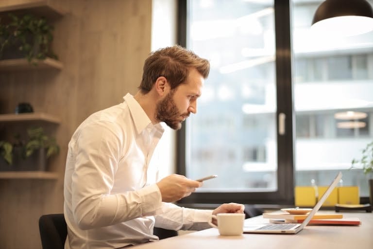 Focused businessman working on laptop while checking how to refinance perth on his smartphone