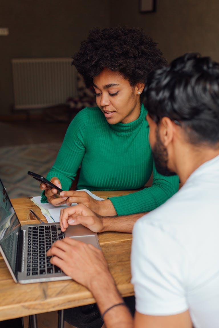 Two adults refinancing their mortgage on a project at home with a laptop and smartphone as they discuss mortgage trends in Perth.