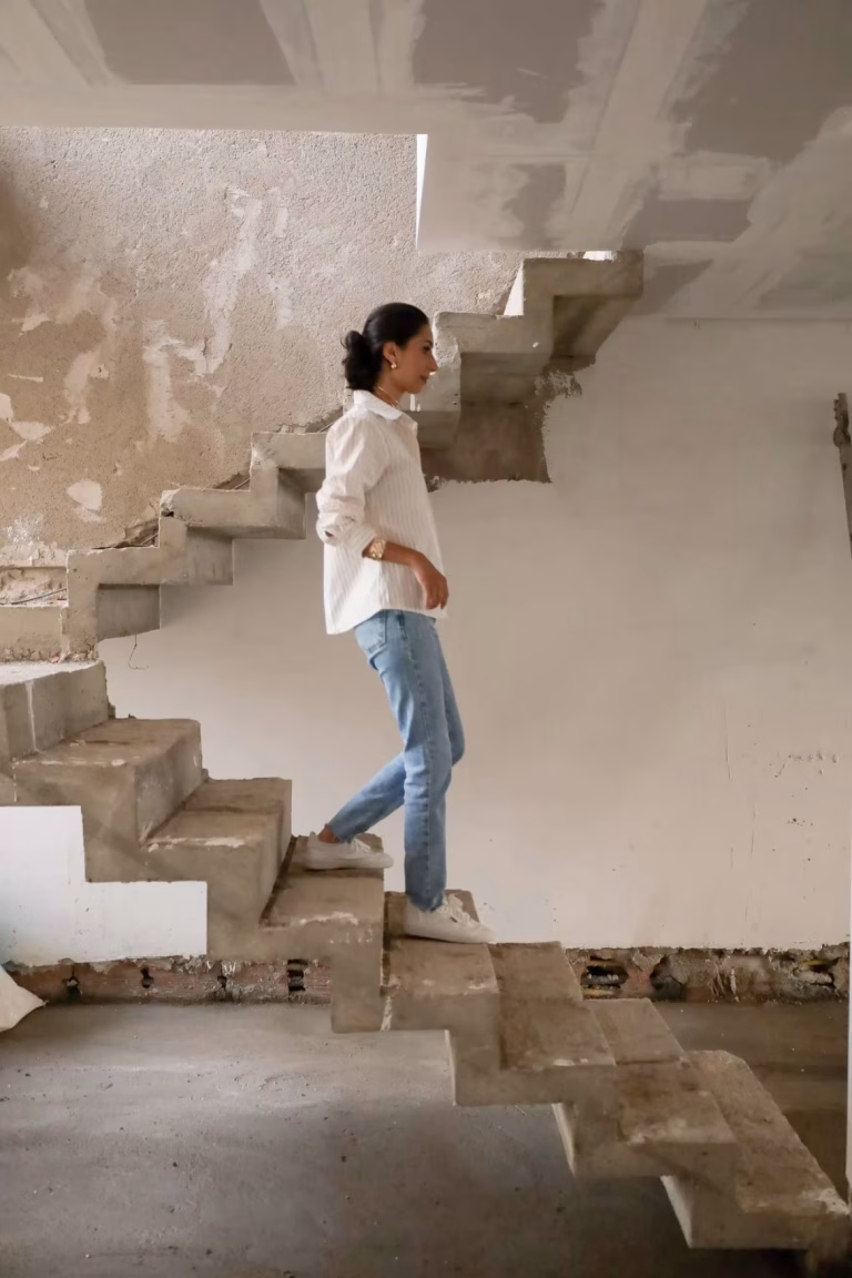 a woman walks down concrete stairs on a construction site during inspection of investment property undergoing renovations