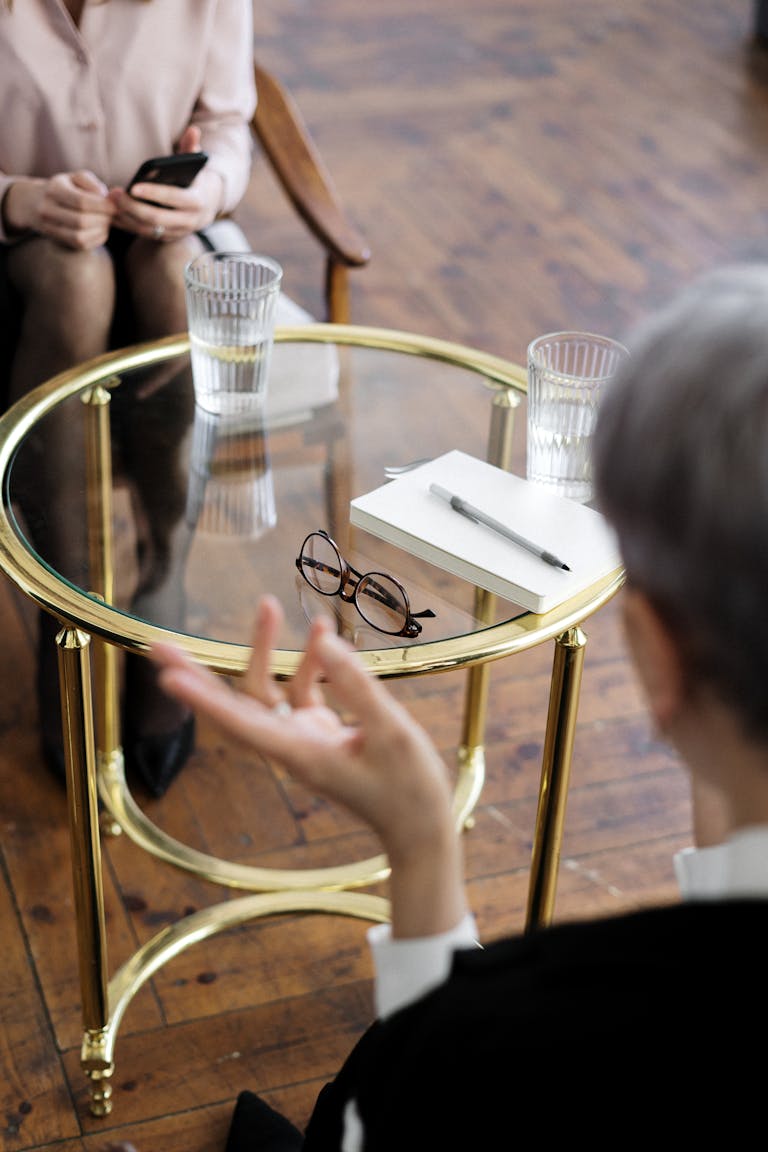 Two adults engaged in a therapy session, seated at a glass table with notebooks and water glasses seeking advice on buying a home after divorce in perth