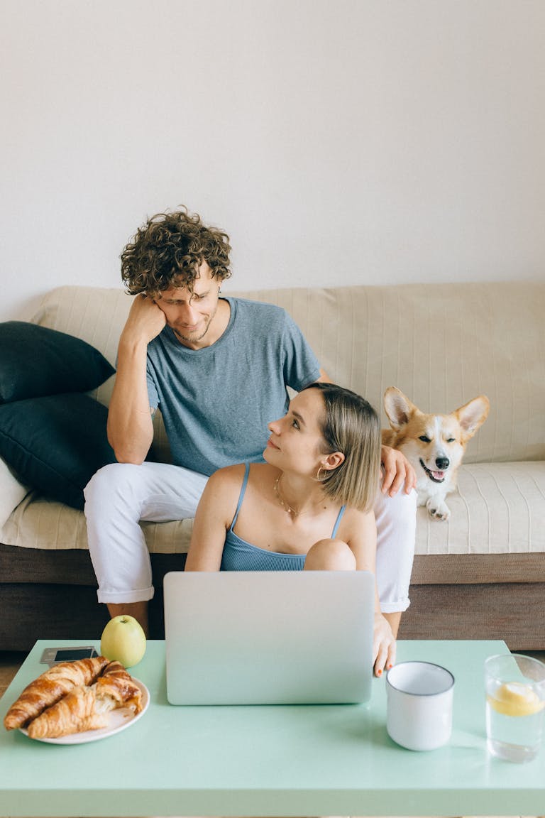 Young couple relaxing in living room with a laptop, enjoying a cozy moment with their dog as they ponder whether to rent vs buy in perth