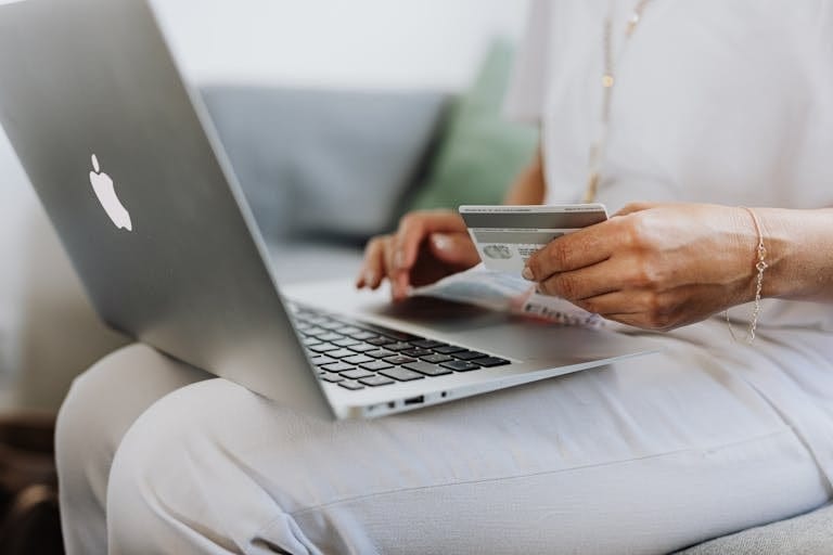 Close-up of a person holding a credit card while shopping online using a laptop at home in the context of living expenses and home loan application.