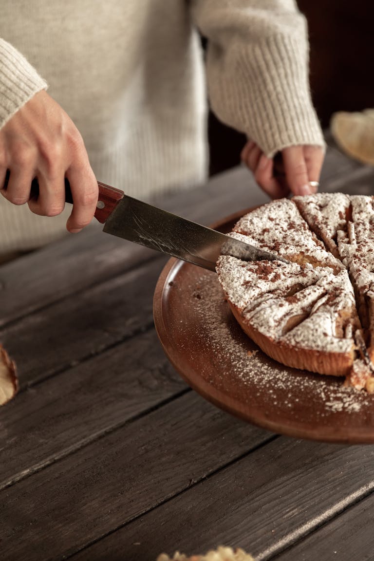 Close-up of a person slicing a freshly baked cake with powdered sugar on a wooden table symbolising the division of assets after divorce when asking can I refinance my home loan to pay out my ex