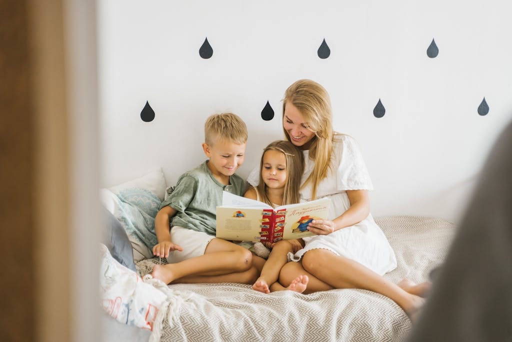 A joyful mother reads a storybook to her young children while sitting on a bed considering options to buy kids a house in Perth