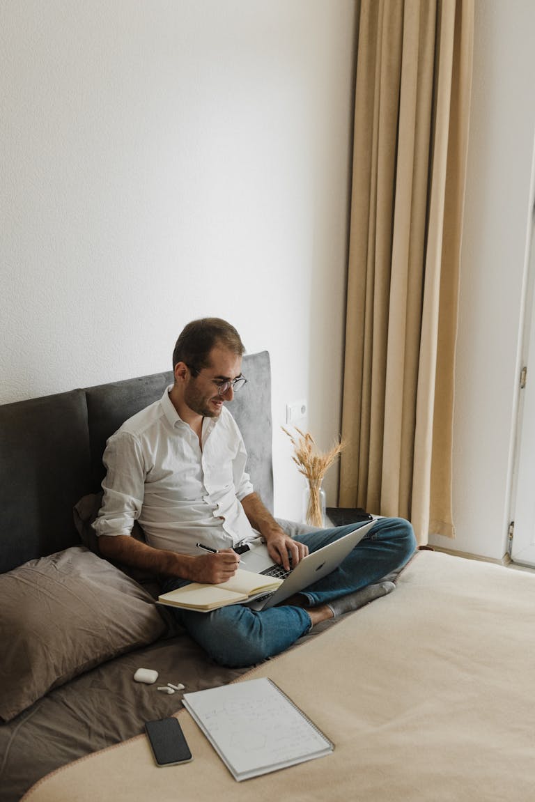 Adult man focused on remote work with laptop and notebook on bed checks his home loan options after speaking with perth mortgage broker