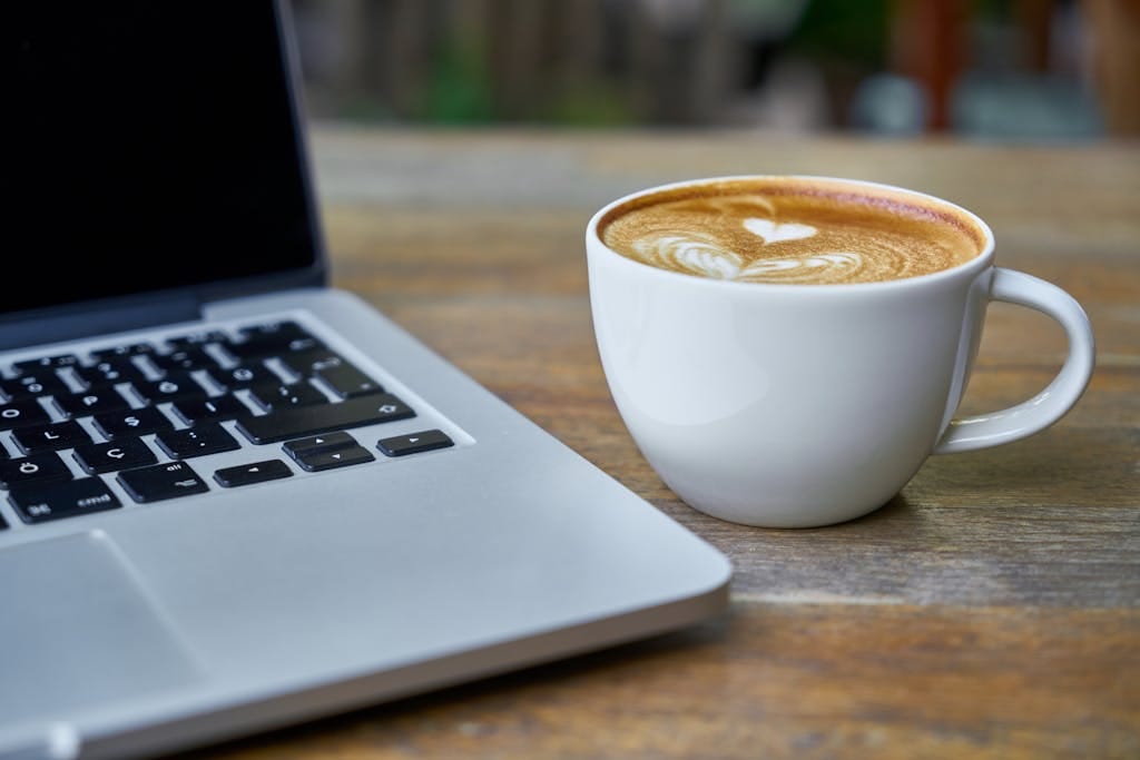Close-up of a latte coffee with heart art next to a laptop on a rustic wooden table for a quick property market update