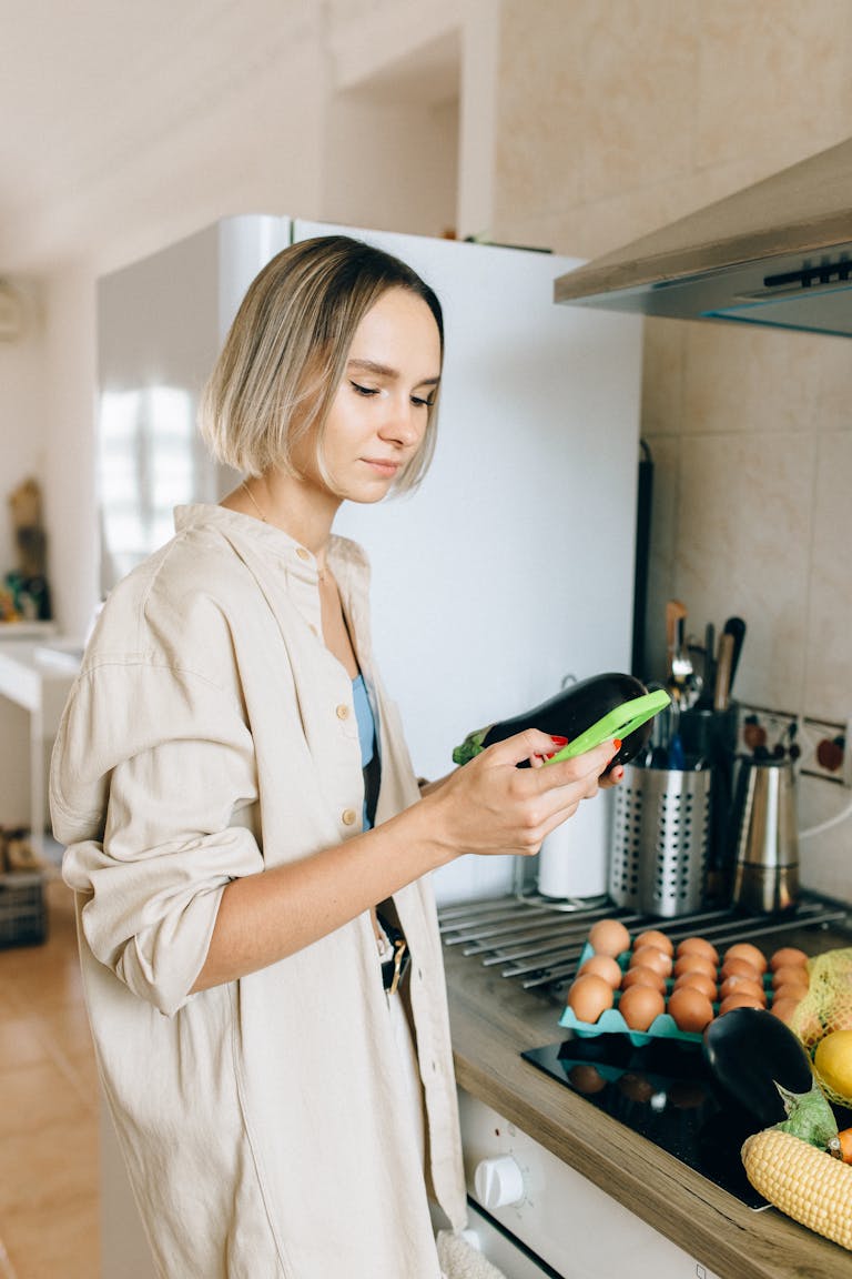 Woman browsing recipes on phone while cooking vegetables and eggs in a bright kitchen as she considers buying before selling in Perth
