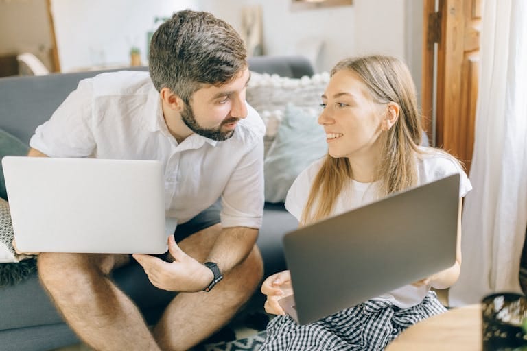 A couple compare refinance options together on their laptops in a cosy living room in Perth