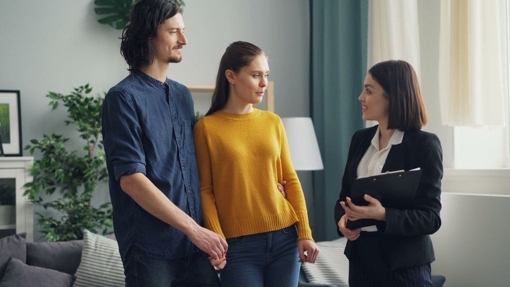 A young couple discusses with a real estate agent in a modern living room setting.