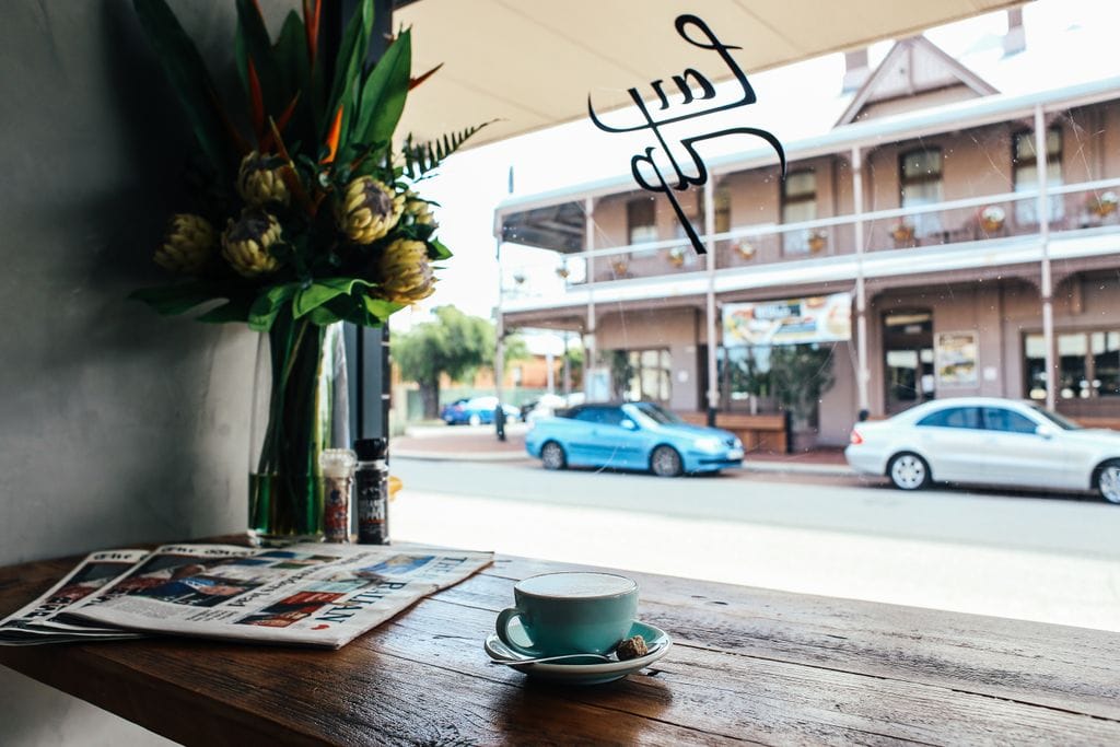A cup of coffee by the window offers a cozy café view of the street outside with flowers and a rustic table in Perth.